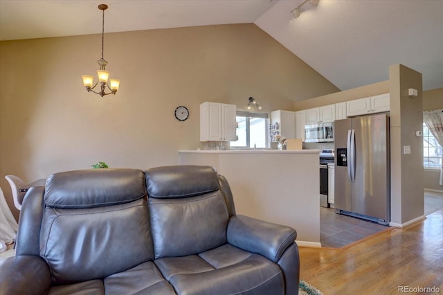 living room with a notable chandelier, wood finished floors, baseboards, and high vaulted ceiling