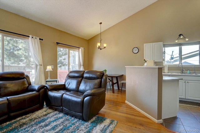 living area with baseboards, vaulted ceiling, wood finished floors, a notable chandelier, and a textured ceiling