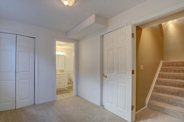 unfurnished bedroom featuring baseboards, a closet, ensuite bathroom, a textured ceiling, and light carpet