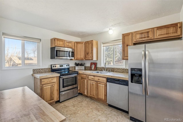 kitchen featuring brown cabinets, stainless steel appliances, a textured ceiling, light countertops, and a sink