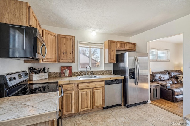 kitchen featuring a textured ceiling, stainless steel appliances, a sink, tile counters, and brown cabinetry