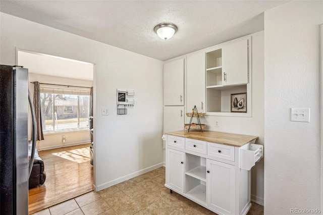 kitchen featuring wood counters, white cabinetry, baseboards, freestanding refrigerator, and open shelves