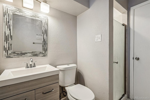 bathroom featuring toilet, vanity, walk in shower, and a textured wall