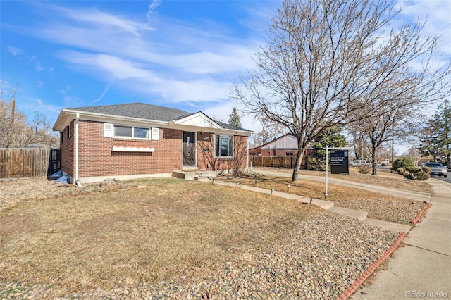 view of front of home with a shingled roof, brick siding, fence, and a front lawn