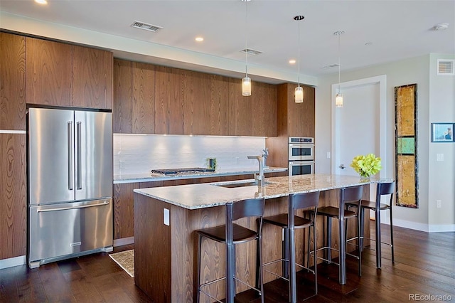 kitchen with appliances with stainless steel finishes, tasteful backsplash, a kitchen island with sink, sink, and hanging light fixtures