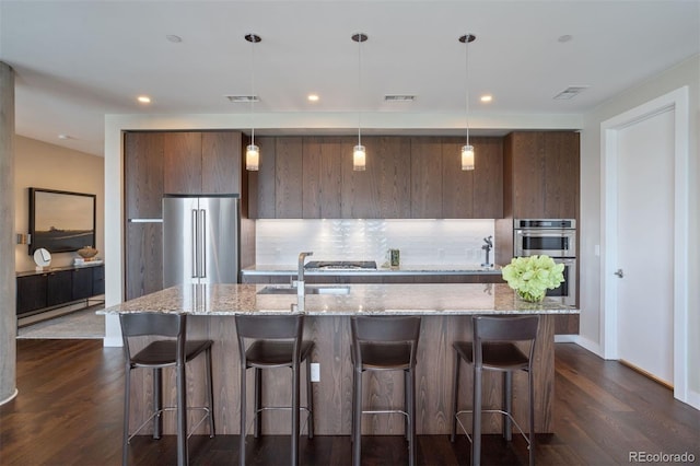 kitchen with backsplash, a center island with sink, hanging light fixtures, and appliances with stainless steel finishes