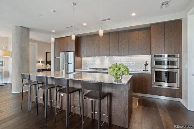 kitchen with hanging light fixtures, decorative backsplash, an island with sink, dark hardwood / wood-style flooring, and stainless steel appliances