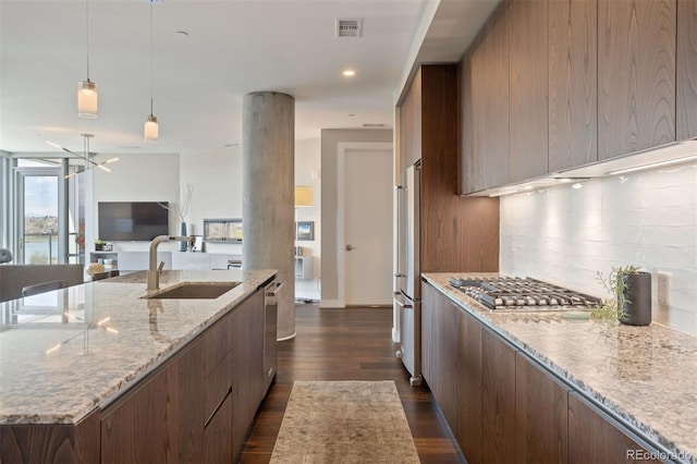 kitchen with a center island with sink, sink, decorative backsplash, light stone countertops, and stainless steel appliances