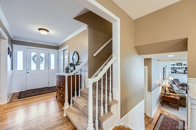 foyer with stairs, crown molding, light wood-style floors, and wainscoting