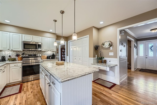 kitchen featuring light stone countertops, a wainscoted wall, stainless steel appliances, light wood-style floors, and a center island