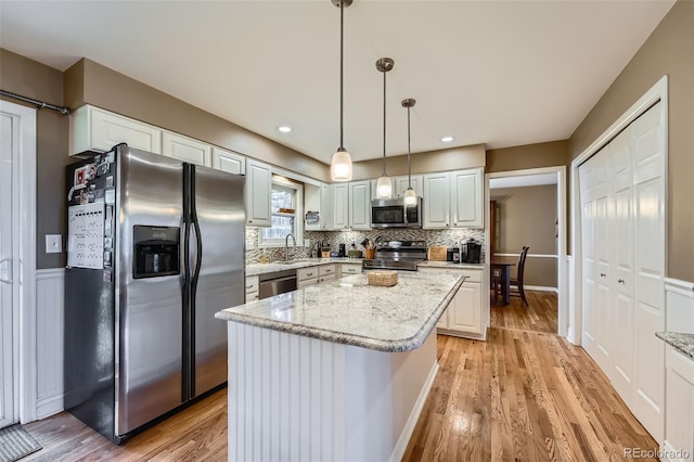 kitchen with a sink, backsplash, light wood-style floors, appliances with stainless steel finishes, and light stone countertops