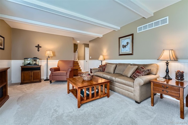 living room with a wainscoted wall, beam ceiling, visible vents, and light carpet