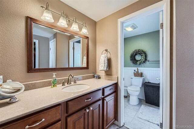 bathroom featuring a wainscoted wall, toilet, and vanity