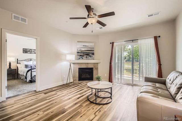 living area with wood finished floors, a tile fireplace, a ceiling fan, and baseboards