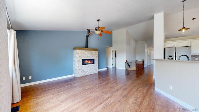 1936 E 144th Dr, Thornton, CO 80602 - unfurnished living room featuring vaulted ceiling, a ceiling fan, wood finished floors, and a brick fireplace