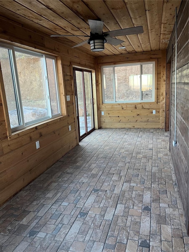 unfurnished sunroom featuring ceiling fan, a healthy amount of sunlight, and wood ceiling