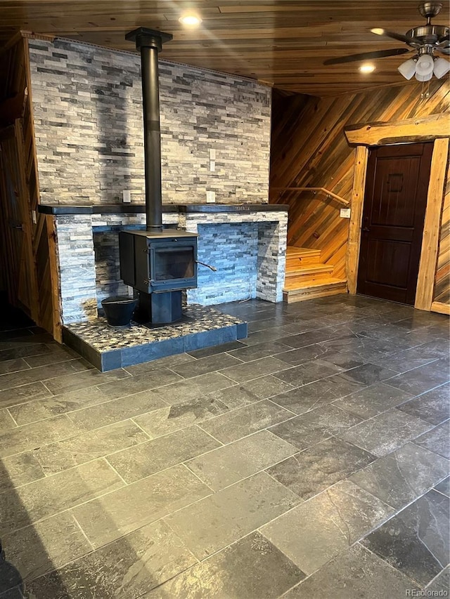 unfurnished living room with ceiling fan, wood walls, wooden ceiling, and a wood stove