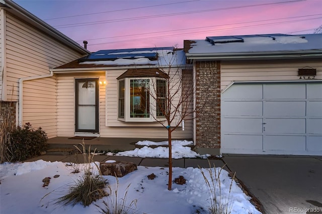 snow covered property entrance featuring a garage and solar panels