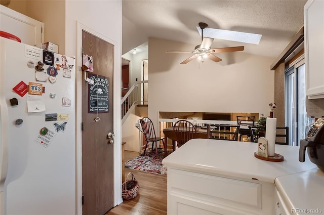 kitchen with ceiling fan, white refrigerator, a textured ceiling, vaulted ceiling with skylight, and white cabinets