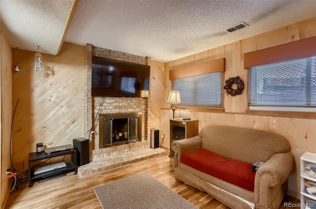 living area with wood walls, a fireplace, a textured ceiling, and light hardwood / wood-style flooring