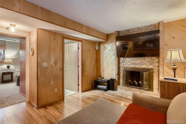 living room featuring light wood-type flooring, a textured ceiling, a brick fireplace, and wood walls