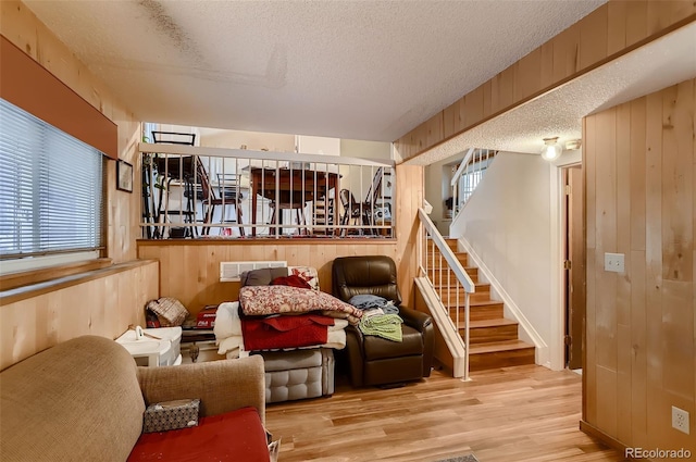 living room with wood walls, a textured ceiling, and light wood-type flooring