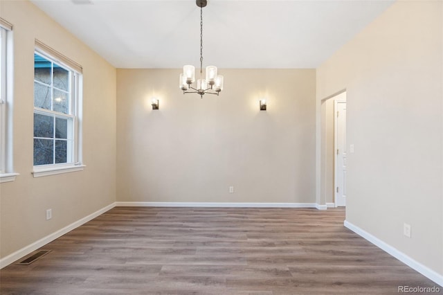 empty room with hardwood / wood-style flooring and an inviting chandelier