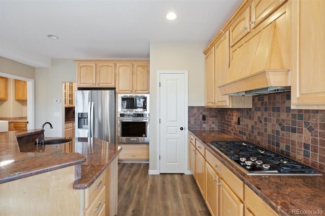 kitchen with appliances with stainless steel finishes, premium range hood, dark wood-type flooring, light brown cabinets, and sink