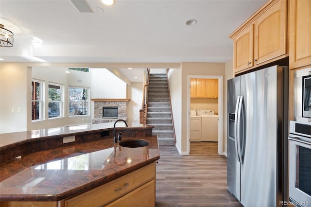 kitchen with sink, appliances with stainless steel finishes, independent washer and dryer, dark stone countertops, and a stone fireplace