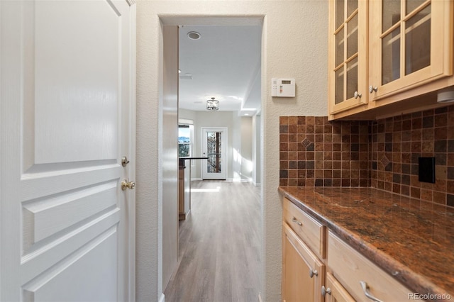 kitchen featuring light hardwood / wood-style floors, dark stone countertops, backsplash, and light brown cabinets