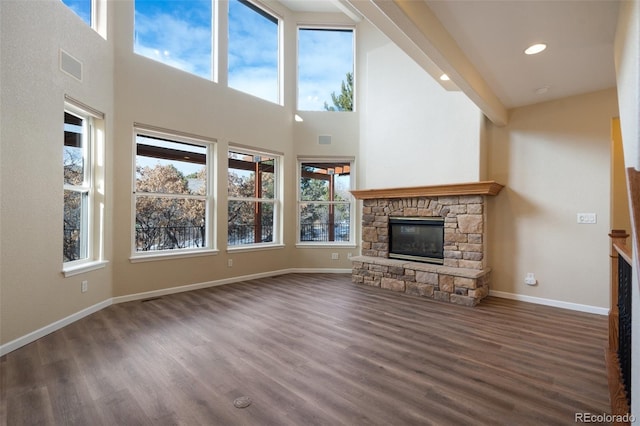 unfurnished living room featuring a towering ceiling, dark wood-type flooring, and a stone fireplace