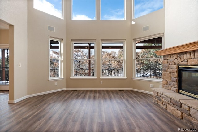 unfurnished living room with dark hardwood / wood-style flooring, a fireplace, a wealth of natural light, and a high ceiling