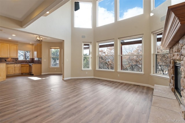 unfurnished living room featuring hardwood / wood-style floors, a towering ceiling, a wealth of natural light, and a stone fireplace