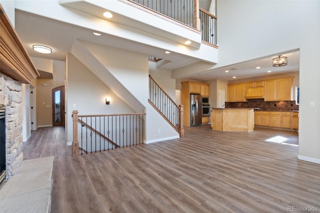 unfurnished living room with hardwood / wood-style floors, a high ceiling, and a stone fireplace