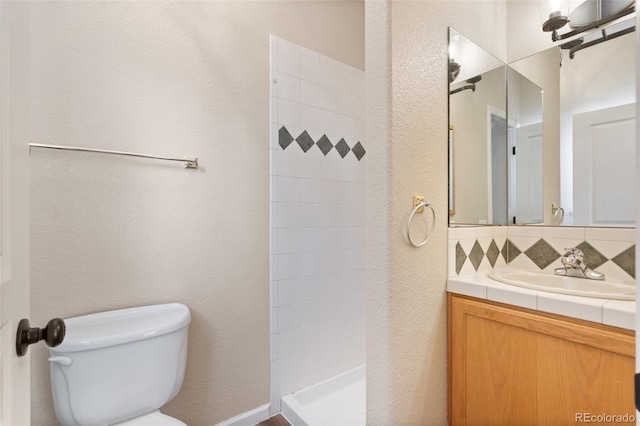 bathroom featuring vanity, a tile shower, tasteful backsplash, and toilet