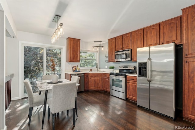 517 Chiswick Cir, Highlands Ranch, CO 80126 - kitchen with stainless steel appliances, brown cabinetry, light countertops, dark wood finished floors, and hanging light fixtures