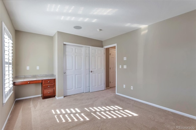 unfurnished bedroom with built in desk, light colored carpet, and a closet