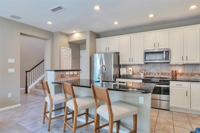 kitchen with a breakfast bar area, a center island with sink, light tile patterned floors, appliances with stainless steel finishes, and white cabinets