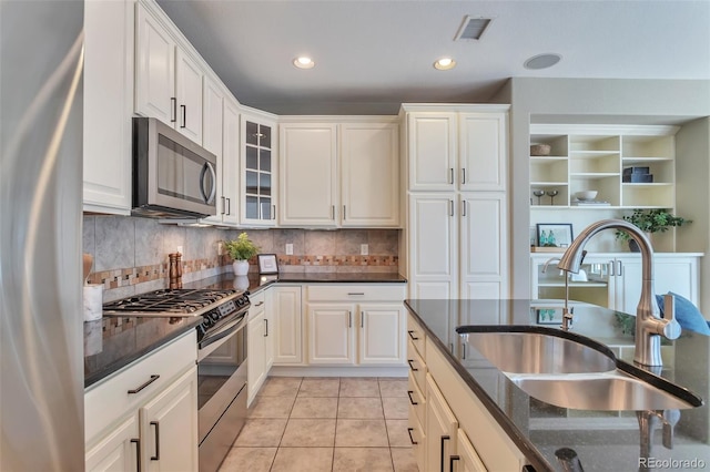 kitchen featuring sink, light tile patterned floors, appliances with stainless steel finishes, dark stone countertops, and white cabinets