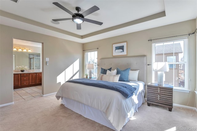 bedroom featuring connected bathroom, light colored carpet, a raised ceiling, and ceiling fan