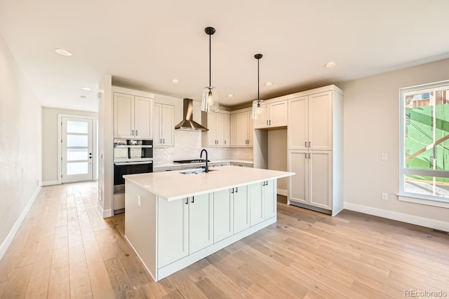 kitchen with a center island with sink, white cabinetry, wall chimney range hood, and decorative light fixtures