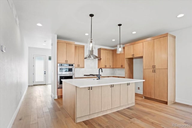 5604 Grandville Ave, Longmont, CO 80503 - kitchen featuring light brown cabinetry, wall chimney range hood, a kitchen island with sink, light countertops, and light wood finished floors