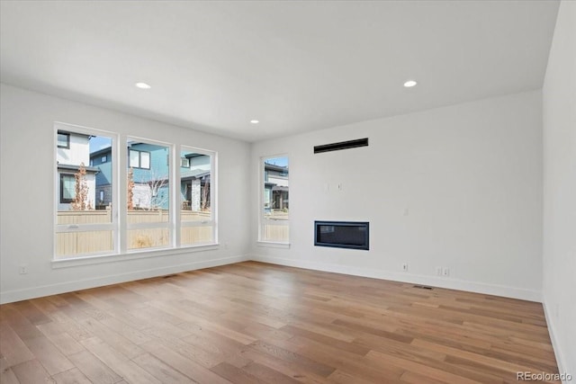 5604 Grandville Ave, Longmont, CO 80503 - unfurnished living room featuring light wood-style flooring, baseboards, a glass covered fireplace, and plenty of natural light