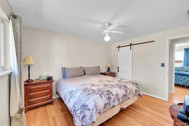 bedroom with baseboards, a barn door, a ceiling fan, and light wood-style floors