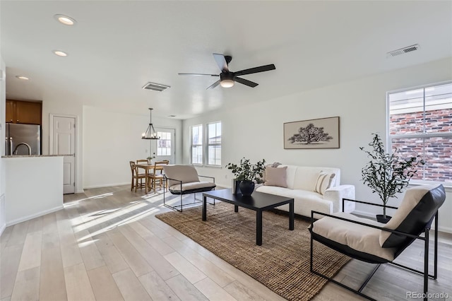 living room with light hardwood / wood-style floors and ceiling fan with notable chandelier