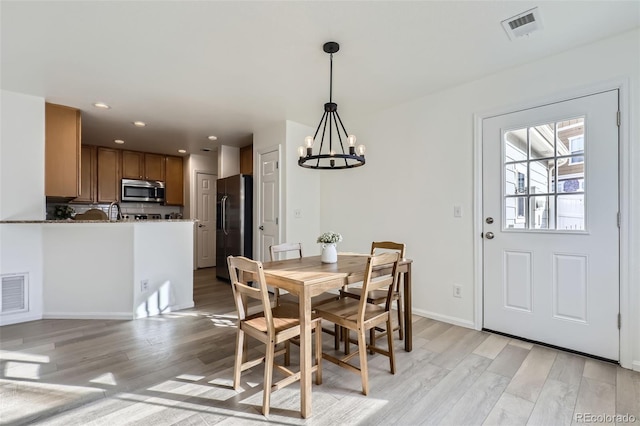 dining space with light wood-type flooring, a notable chandelier, and sink