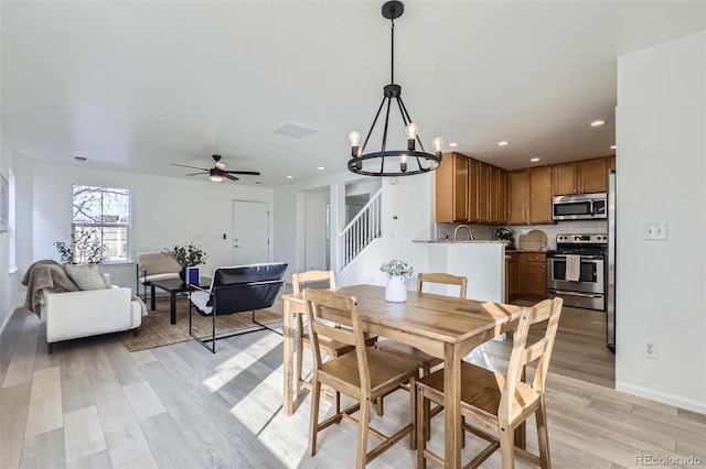 dining room featuring ceiling fan with notable chandelier and light hardwood / wood-style flooring