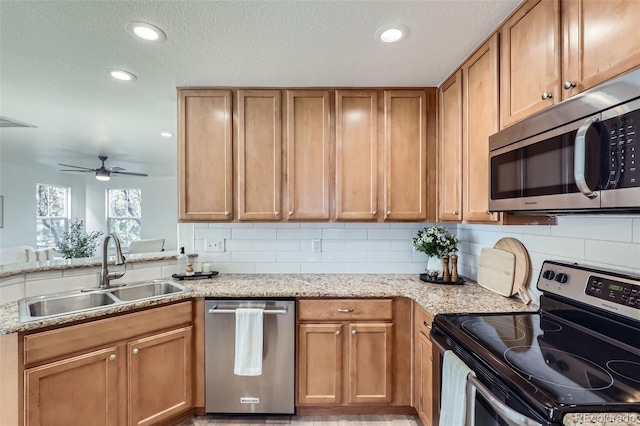 kitchen with light stone countertops, stainless steel appliances, tasteful backsplash, sink, and ceiling fan