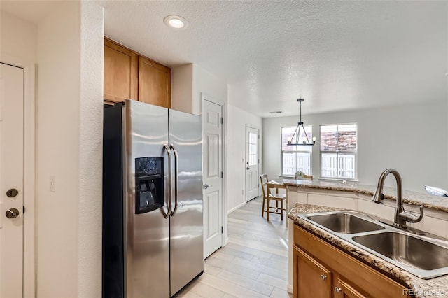 kitchen with pendant lighting, stainless steel refrigerator with ice dispenser, sink, a textured ceiling, and a chandelier