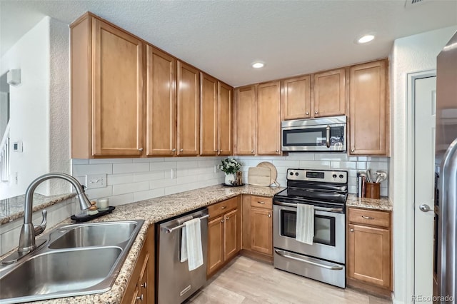 kitchen featuring light stone countertops, stainless steel appliances, tasteful backsplash, sink, and light hardwood / wood-style flooring